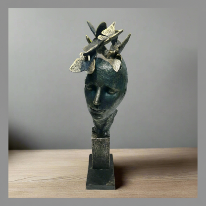 Bronze sculpture of a face with butterflies on a gray background