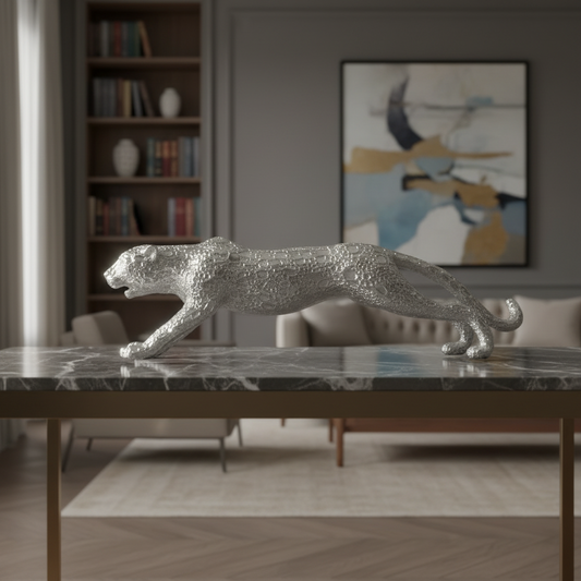 A silver metallic leopard figurine with a textured, glittering finish, posed in a dynamic crouching stance on a dark marble-topped table in a modern, stylishly decorated living room.