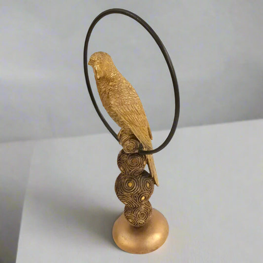 A decorative sculpture featuring a golden bird perched atop a collection of textured gold-colored spheres, with a sleek black metal ring encircling the spheres.
