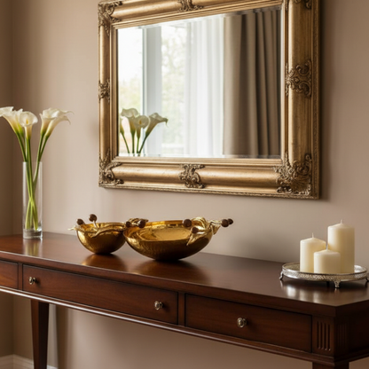 Decorative table with gold bowls, white candles, and a vase of flowers, featuring an ornate mirror.