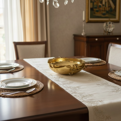 Dining table set with a gold bowl, plates, and cutlery in a room with curtains and a painting.