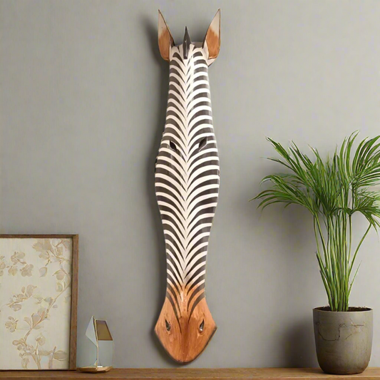 Wooden zebra head wall decoration on a gray wall with a plant and framed picture.