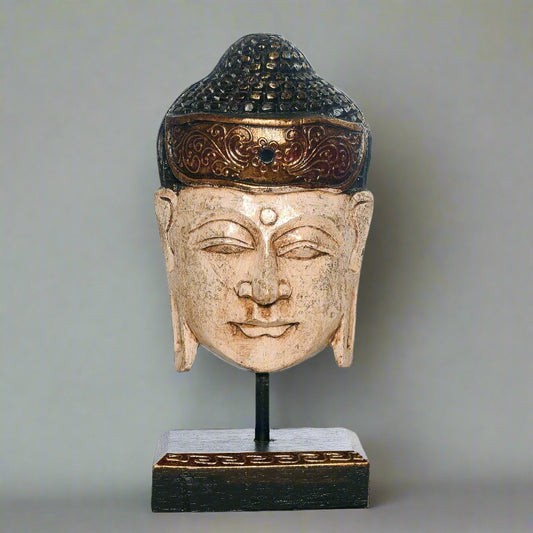 Buddha head sculpture with ornate headdress on a stand against a plain background