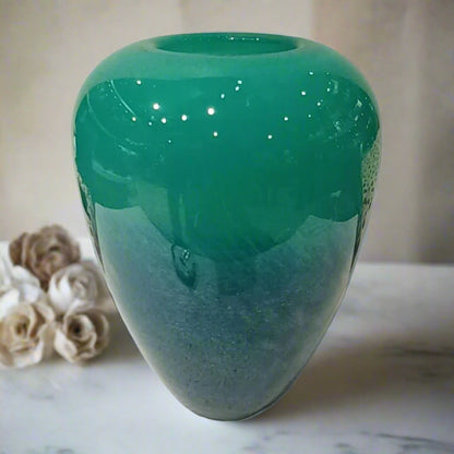 Green glass vase on a light surface with a blurred background