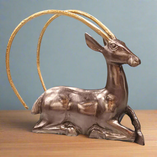 Metallic deer figurine with a gold antler on a wooden surface and blue background