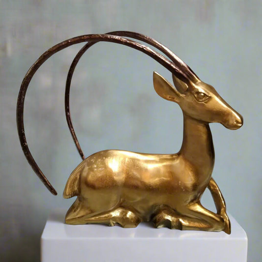 Gold antelope figurine on a white pedestal with a light gray background