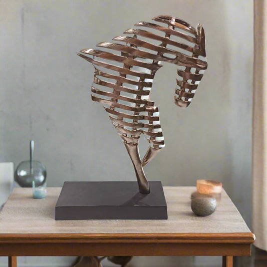Metallic sculpture of a horse on a wooden table with a neutral background