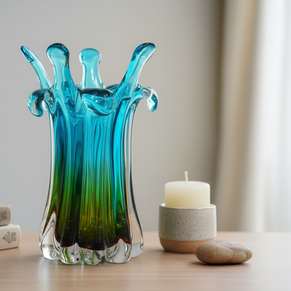 Blue and green glass vase on a wooden surface with a candle and stone in the background