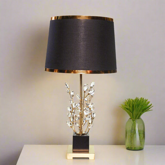 Decorative table lamp with black shade and gold base on a white background
