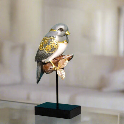 Decorative bird sculpture with gold accents on a stand in a blurred indoor setting