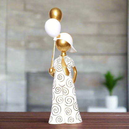 Decorative figurine of a woman holding a white balloon with gold accents on a wooden surface.