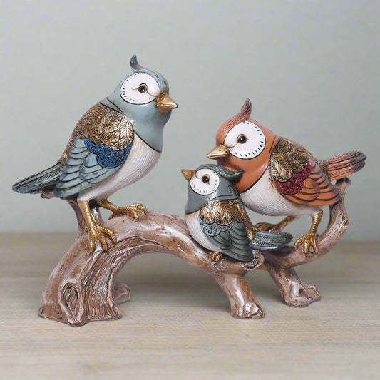 Decorative figurines of three birds on a branch against a plain background