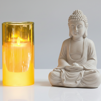 White Buddha statue next to a yellow candle on a light gray background