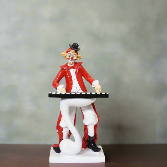 Clown figurine in a red suit with a top hat holding a keyboard on a wooden surface.