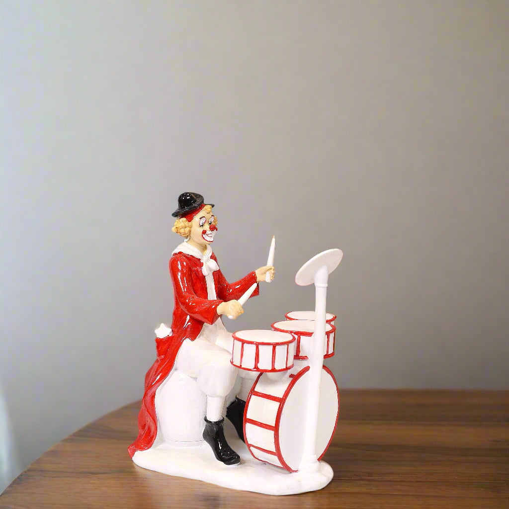 Clown figurine playing drums on a plain background