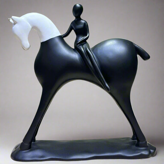 Black and white sculpture of a horse with a rider on a wooden surface and green background
