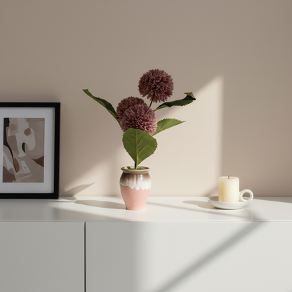 Vase with purple flowers and a candle on a white surface against a beige wall.
