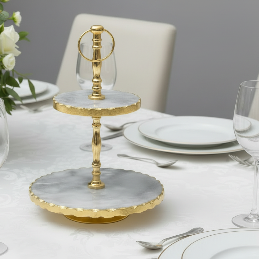 Gold and marble two-tiered stand on a table setting with plates and glasses.
