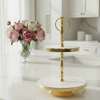 Gold cake stand on a kitchen counter with flowers in the background