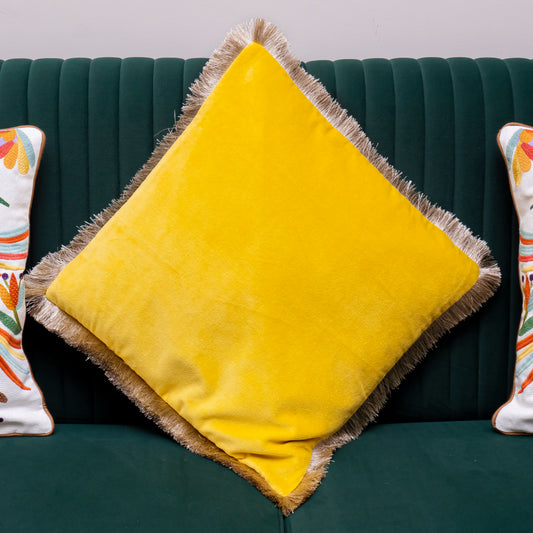 Yellow pillow with frayed edges on a green couch with other decorative pillows.