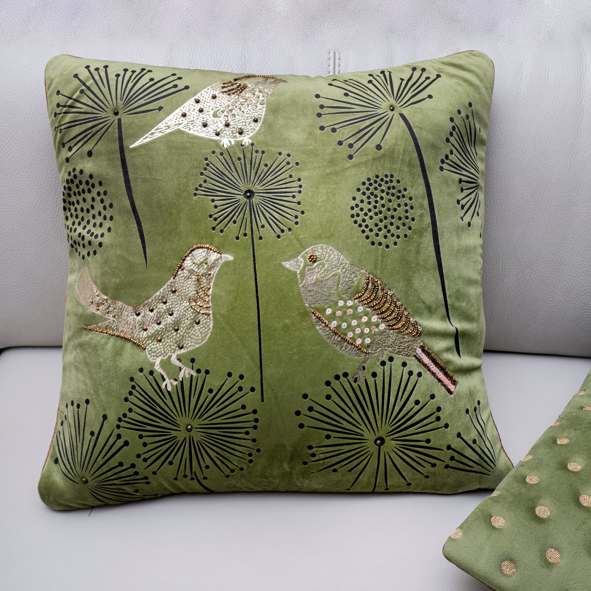 Green pillow with bird and dandelion design on a light gray background
