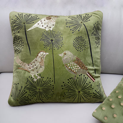 Green pillow with bird and dandelion design on a light gray background
