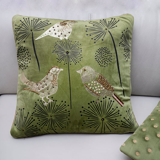 Green pillow with bird and dandelion design on a light gray background