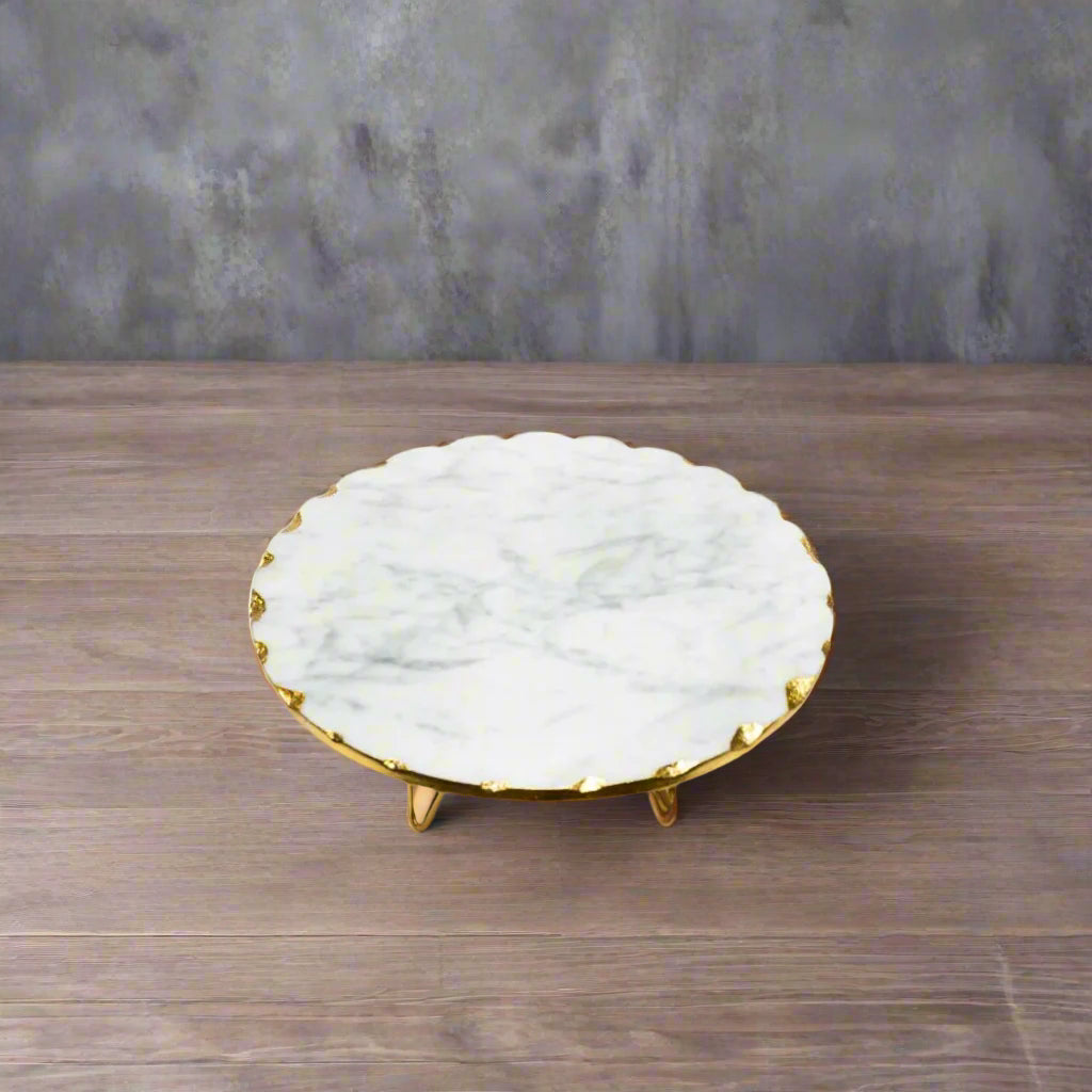Marble cake stand with gold rim on a white surface, with flowers in the background.