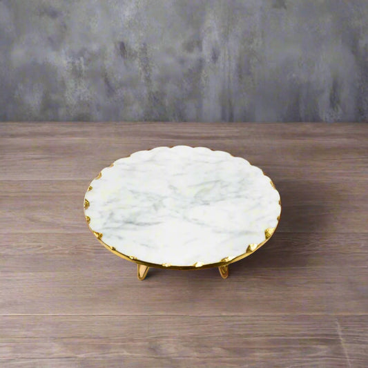 Marble cake stand with gold rim on a white surface, with flowers in the background.