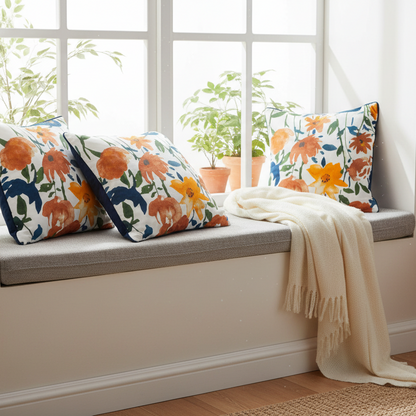 Decorative pillows with floral patterns on a window seat with a blanket.