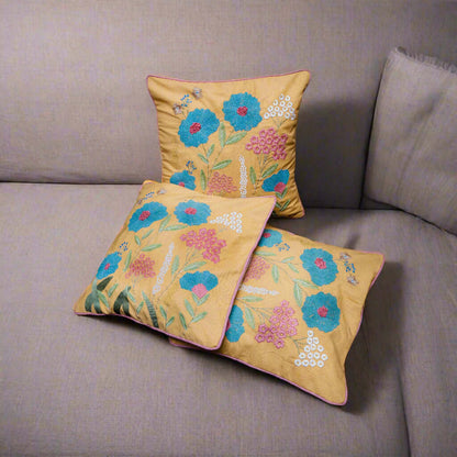 Three embroidered pillows with floral patterns on a gray sofa.