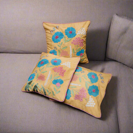 Three embroidered pillows with floral patterns on a gray sofa.