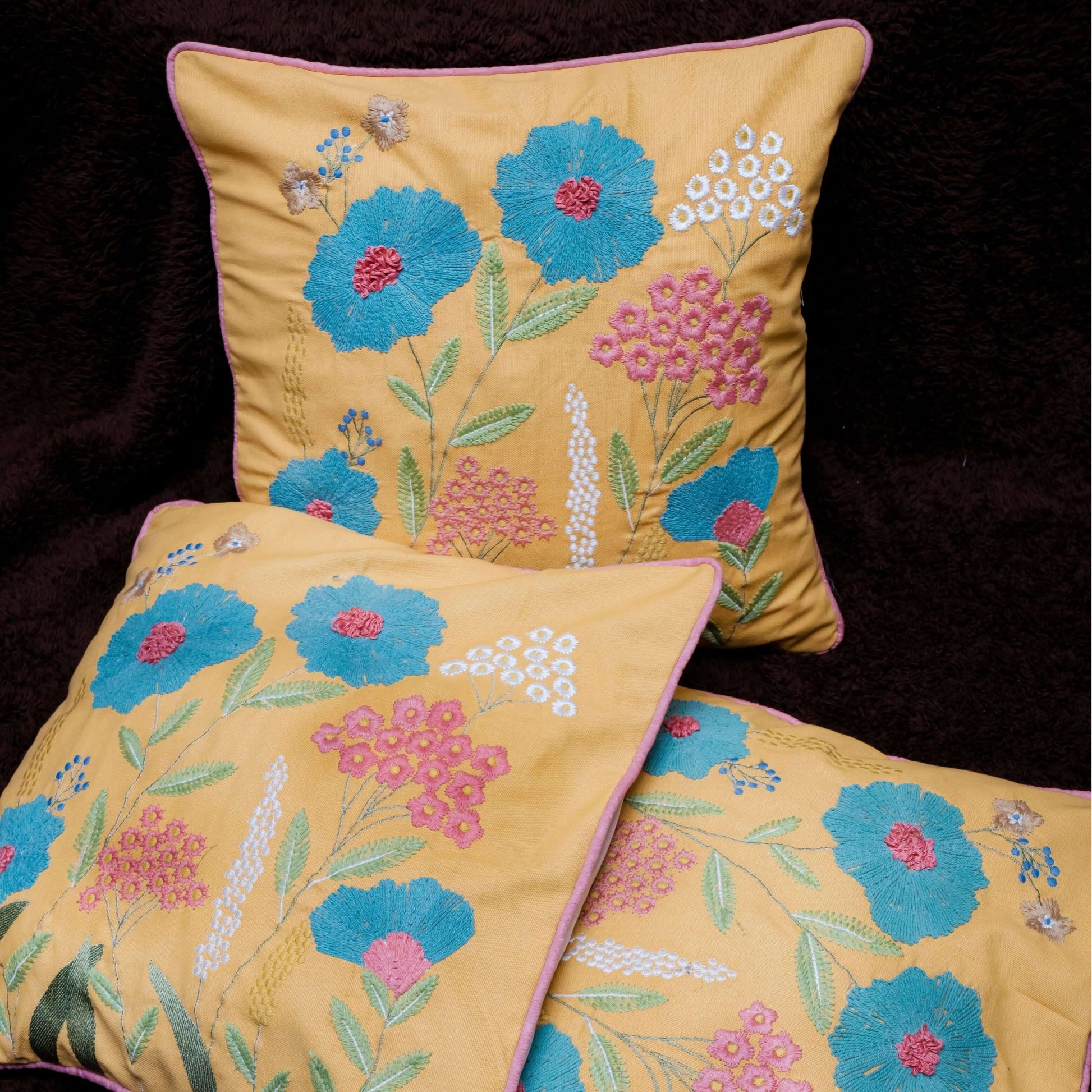 Three embroidered pillows with floral patterns on a dark background