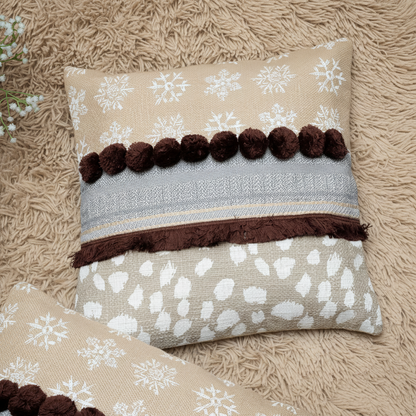 Decorative pillow with snowflake pattern and brown pom-poms on a textured surface