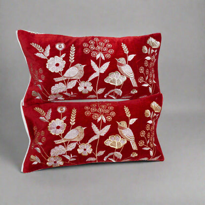 Two red pillows with gold floral and bird patterns on a white background
