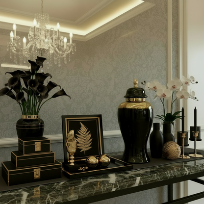 Black and gold decorative vase on a marble surface with a plant and books in the background.