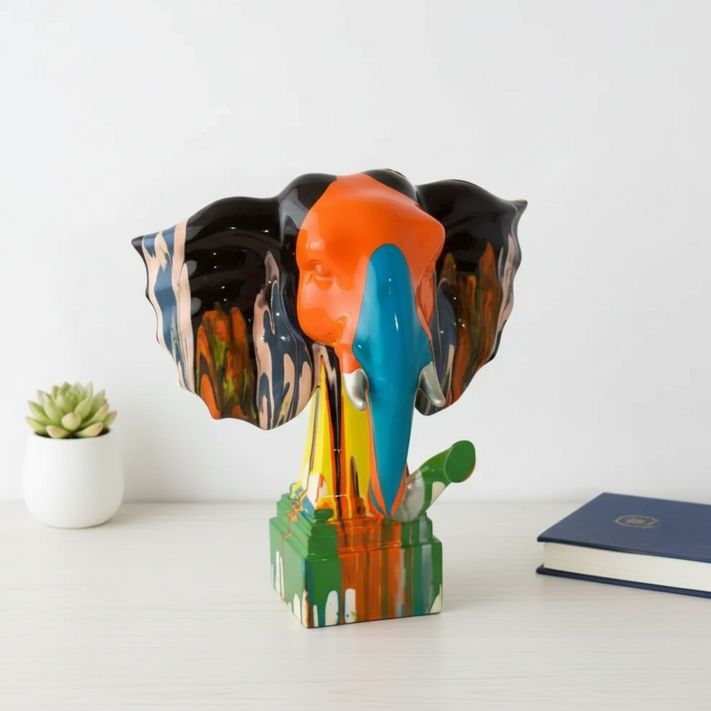 Colorful elephant sculpture on a white surface with a plant and book in the background