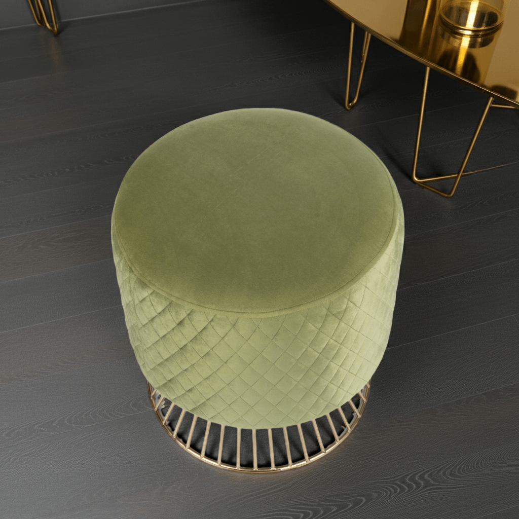 Green velvet ottoman on a dark wooden floor with a gold side table in the background.