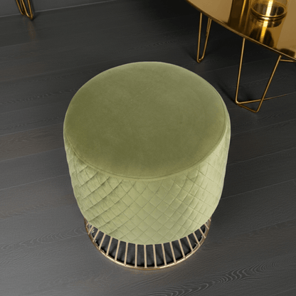 Green velvet ottoman on a dark wooden floor with a gold side table in the background.