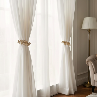 White curtains with gold decorative ties in a room with a lamp and chair.