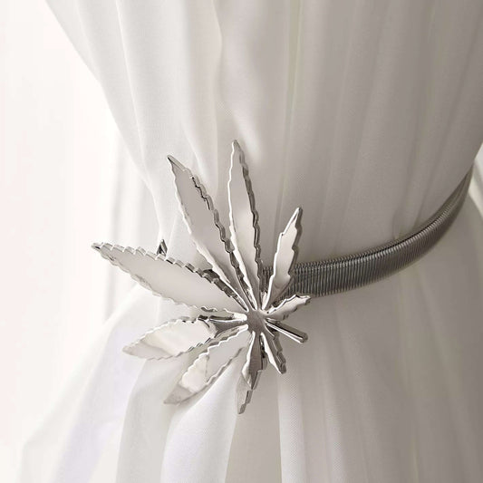 Silver belt buckle shaped like a cannabis leaf on a white dress.