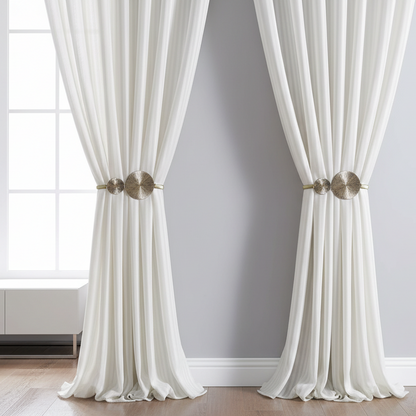 White curtains with gold tiebacks in a room with a light gray wall and wooden floor.