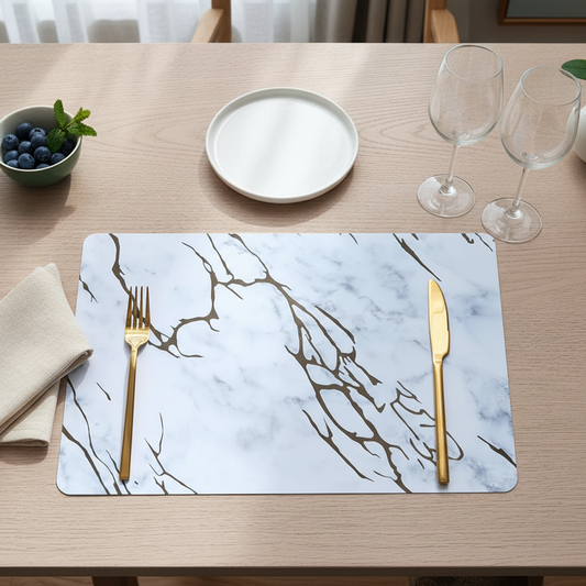 Dining table setting with marble placemat, gold fork and knife, and white plate.