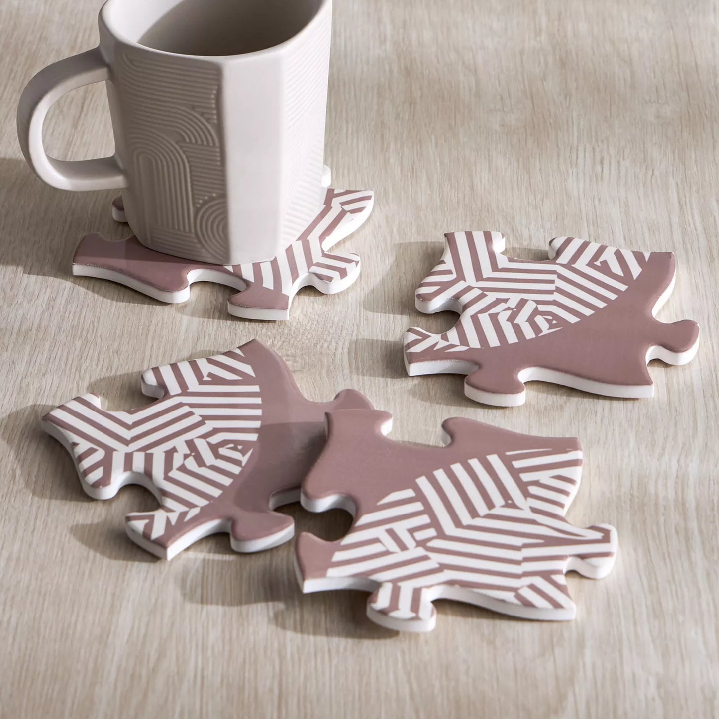 Set of four pink and white patterned coasters on a wooden surface with a mug.