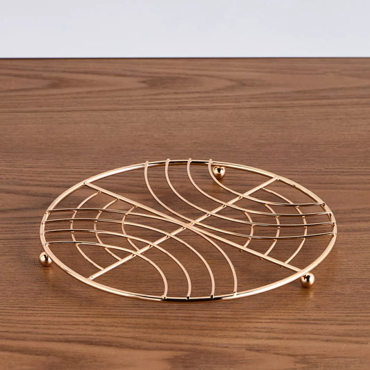 Gold decorative metal trivet on a wooden surface