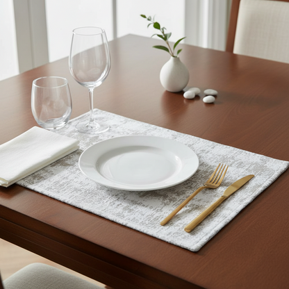 Dining table setting with white plate, gold fork and knife, and clear glasses on a placemat.