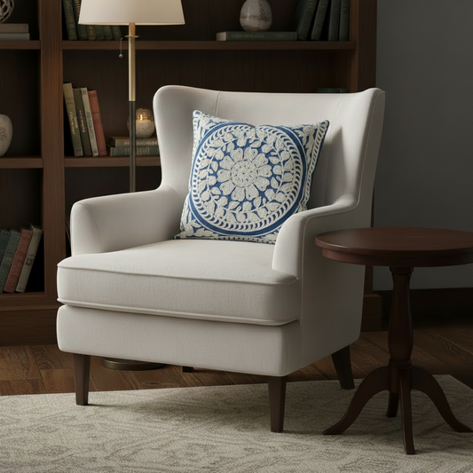 White armchair with a blue and white patterned pillow in a room with a bookshelf and side table.