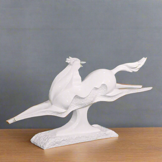 White ceramic sculpture of a horse on a table with a blurred green outdoor background