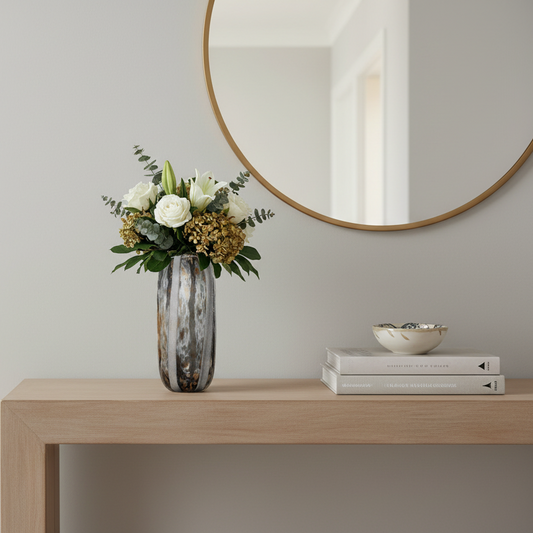 Vase with flowers on a wooden table in a room with a mirror and books.