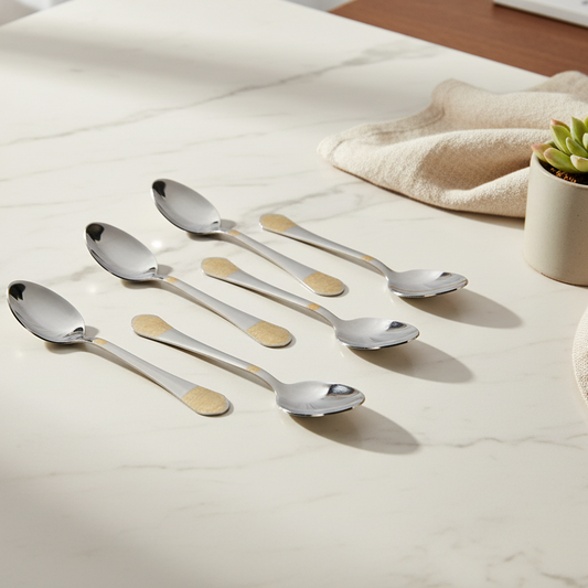 Set of six silver spoons with gold accents on a light surface.